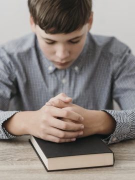 boy-praying-with-his-hands-on-bible